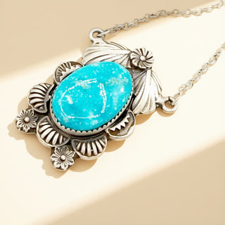 Necklace with a turquoise stone and silver floral design on a beige background