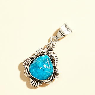 Turquoise stone pendant with silver decorative elements on a beige background