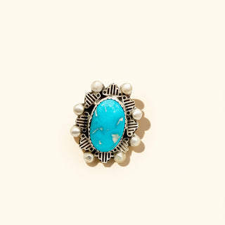 Jewelry item with turquoise stone and pearl-like accents on a beige background