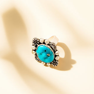 Ring with turquoise stone and silver detailing on a beige background