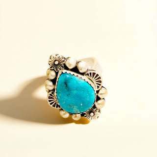 Ring with turquoise stone and silver accents on a beige background