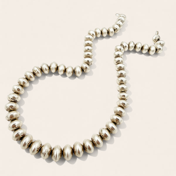 A sterling silver beaded necklace with textured beads and a matching lobster clasp, displayed on a light beige background.