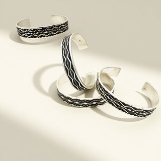 Four silver cuffs with intricate designs on a beige background