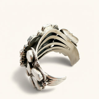 A wide sterling silver cuff bracelet featuring a detailed floral and leaf design with a ribbed texture, photographed on a clean, light beige background.