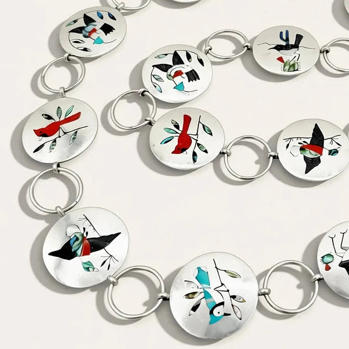 A silver-toned circular link chain necklace featuring multiple round white inlaid discs decorated with abstract black, red, and turquoise geometric and bird-like motifs, arranged on a light neutral background.