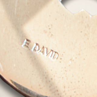 close up of silver jewelry with 'E. DAVID' engraved on a beige background