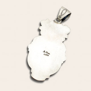 Silver pendant with engraved design on a light pink background
