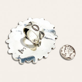 Silver ring with engraved design on a decorative stand next to a penny for scale.