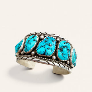 A Southwestern-style cuff bracelet featuring five oval turquoise stones set in a textured silver-tone metal band with decorative rope and wave details, photographed on a clean off-white background.