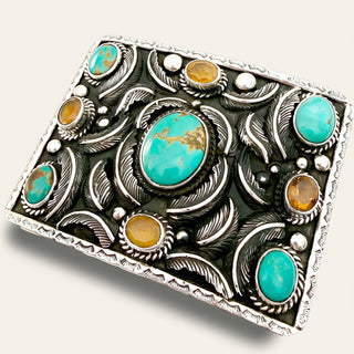 Decorative silver belt buckle with turquoise and amber stones on a white background