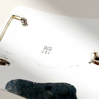 Close-up of a silver ring with 'JCV' engraved on it, placed on a white surface.