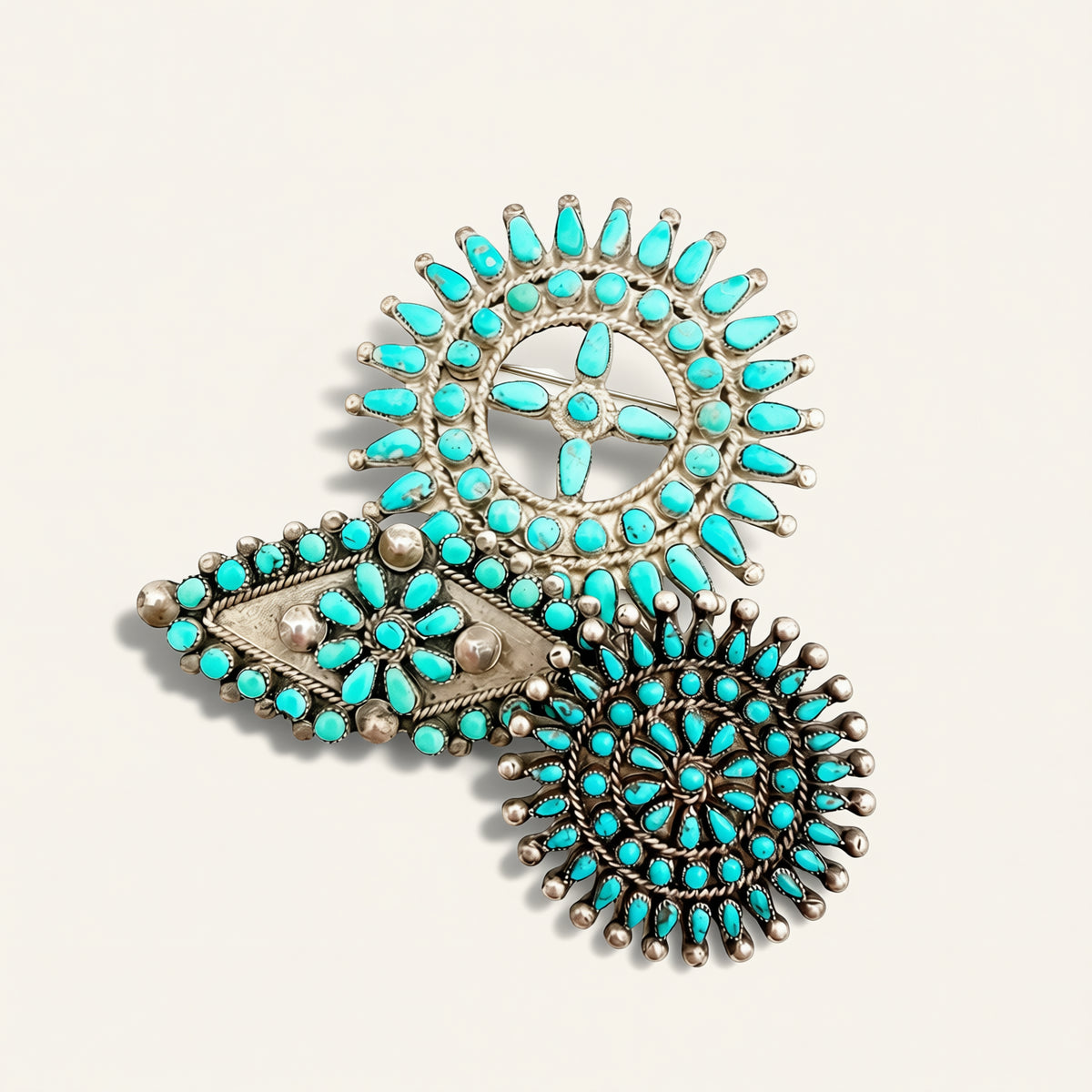 A set of three silver-toned Native American style turquoise jewelry charms, including sunburst, diamond, and circular designs, arranged on a light beige background.