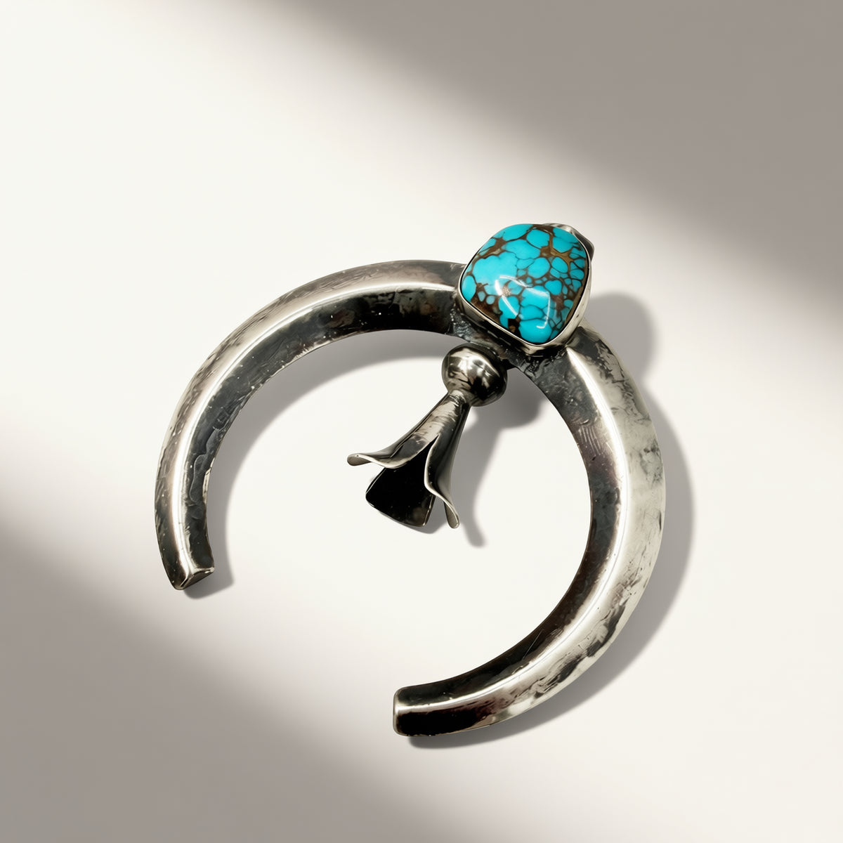 Silver crescent-shaped pendant with a turquoise stone on a white background