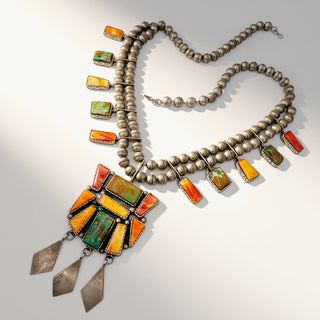 A Southwestern-style silver necklace with a large geometric pendant featuring orange, green, and yellow stones, accented by smaller matching stone and bead drops on a white background.