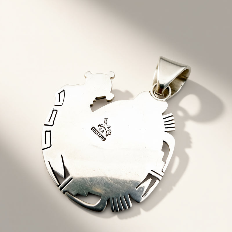 A sterling silver pendant shaped like a stylized animal head with cutout details, shown on a light beige background with a soft shadow. The pendant features a polished finish and a small 'sterling' hallmark stamped on the side.