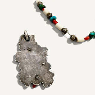 A silver pendant necklace with a textured, organic leaf-like shape, shown next to a matching beaded strand on a light gray background.