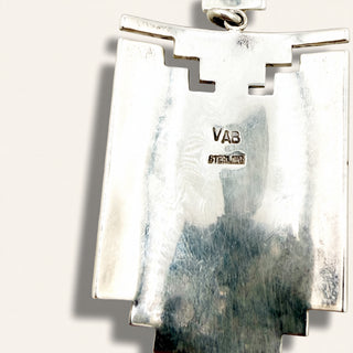 Close-up of a silver pendant with a stepped geometric design, showing a sterling silver hallmark and a hanging loop at the top, set against a plain off-white background.