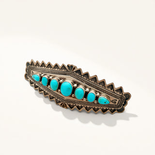A silver-toned Southwestern-style jewelry  featuring a row of oval turquoise stones on a textured, engraved background, photographed on a clean off-white surface.