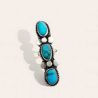 A silver-toned Southwestern-style ring featuring three vertical rows of oval turquoise stones, accented with small round silver beads, photographed on a light beige background with a soft shadow.