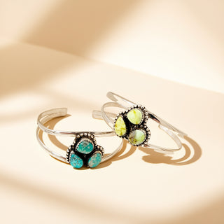 Two silver cuffs with three stones on a beige background