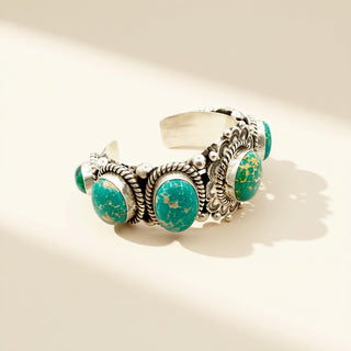 Silver cuff with green stones on a beige background