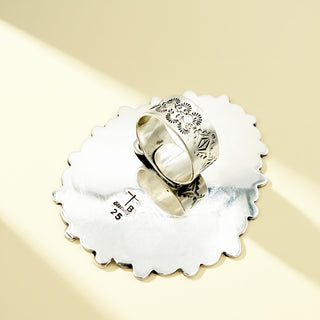 Silver ring with intricate design on a matching silver stand against a beige background
