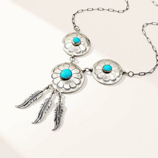 Silver necklace with turquoise stones and feather pendants on a white background