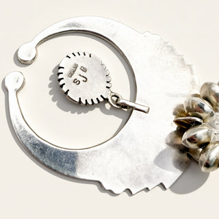 Silver jewelry with a circular tag and floral design on a white background