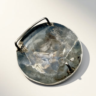 A round jewelry piece and a silver-toned handle, photographed on a clean white background.