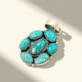 Turquoise stone pendant with silver setting on a beige background