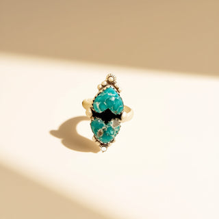 Turquoise ring with gold accents on a beige background