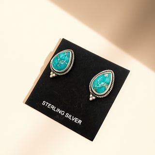Turquoise earrings on a black card labeled 'Sterling Silver' with a beige background