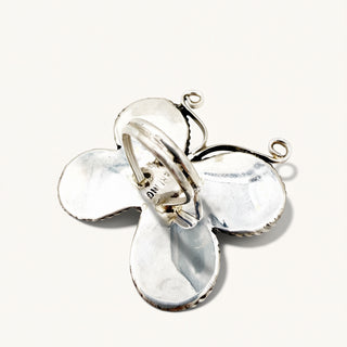 A sterling silver butterfly-shaped pendant with a textured, hammered finish and two small jump rings for hanging, shown on a light cream background.