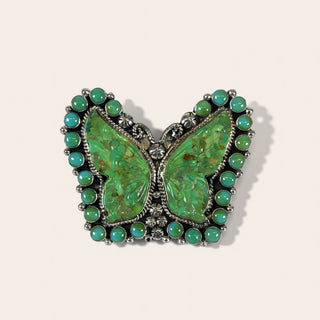 Butterfly-shaped brooch with green gemstones on a beige background